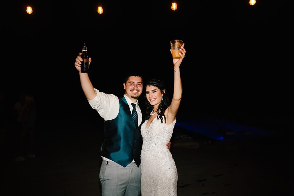 bride and groom hold up their drinks for a photo at their backyard wedding reception photographed by Kansas City photographer Natalie Nichole Photography