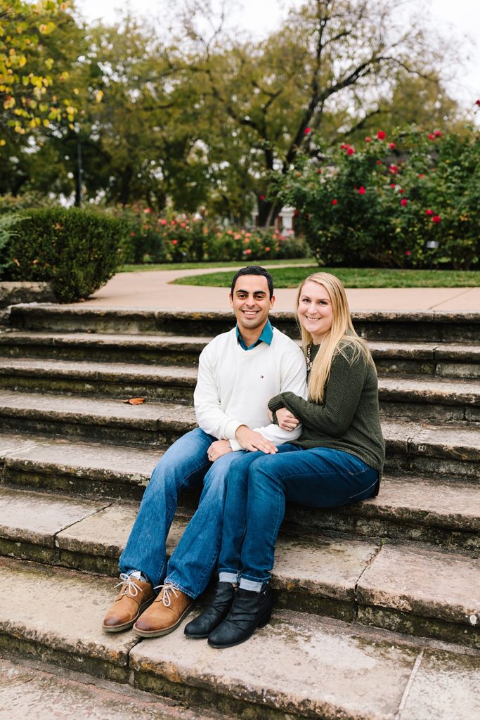 fall couples photos at loose park in kansas city, couple sits on steps in rose garden