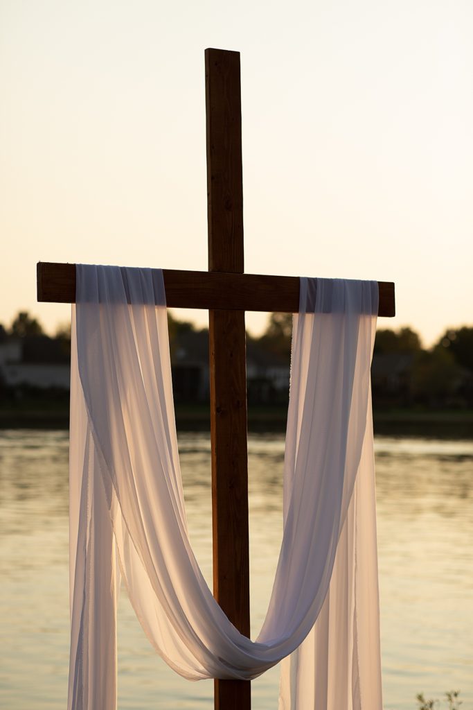 handmade wooden cross for wedding ceremony draped with white fabric at intimate elopement at Raintree Lake in Lee's Summit Kansas City at golden hour in October