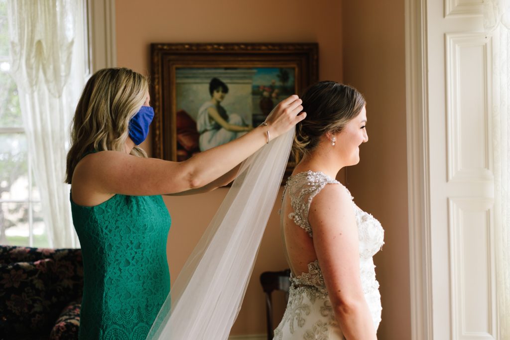 bride's sister wears a mask while helping her put on her veil