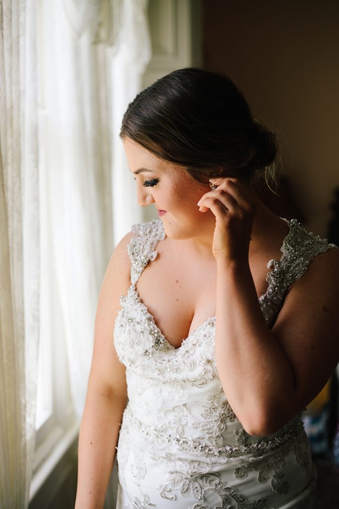 bride wearing wedding dress designed by Maggie Sottero putting on her earrings