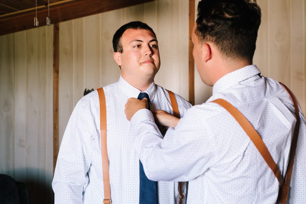groom getting ready, navy tie, brown suspenders, summer wedding at The Barn at Cricket Creek