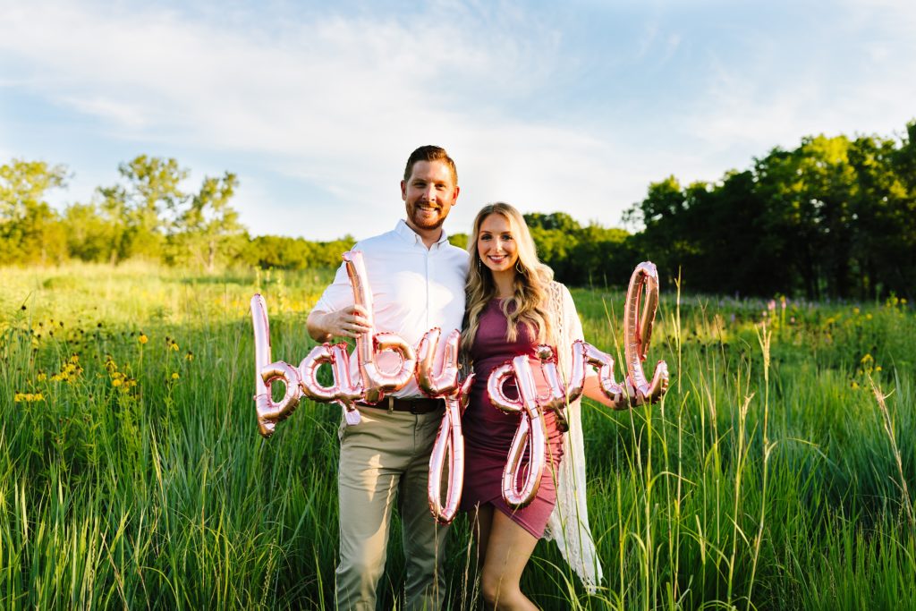 sunrise maternity session at Shawnee Mission Park, Kansas City Photographer, baby girl balloons, rose gold baby girl sign, rose gold, balloon garland, wild flowers, maternity photos in open field, green grass, pink dress, gender reveal