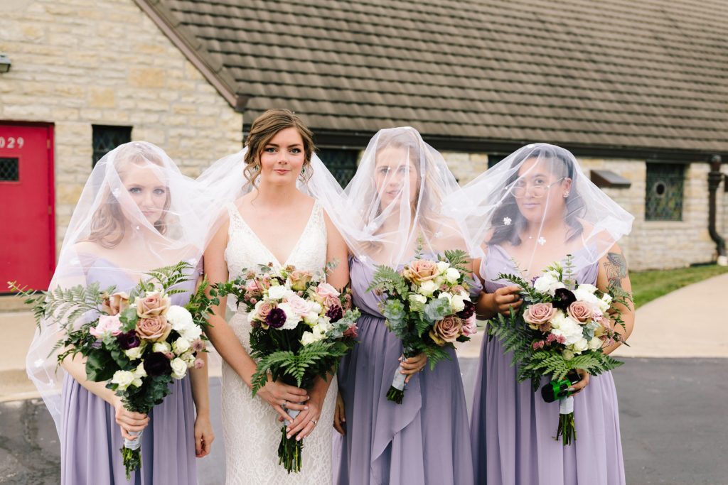 edgy bridal party, trendy bridesmaids, lavender bridesmaids dresses, large bouquet, bridesmaids under brides veil, homemade veil