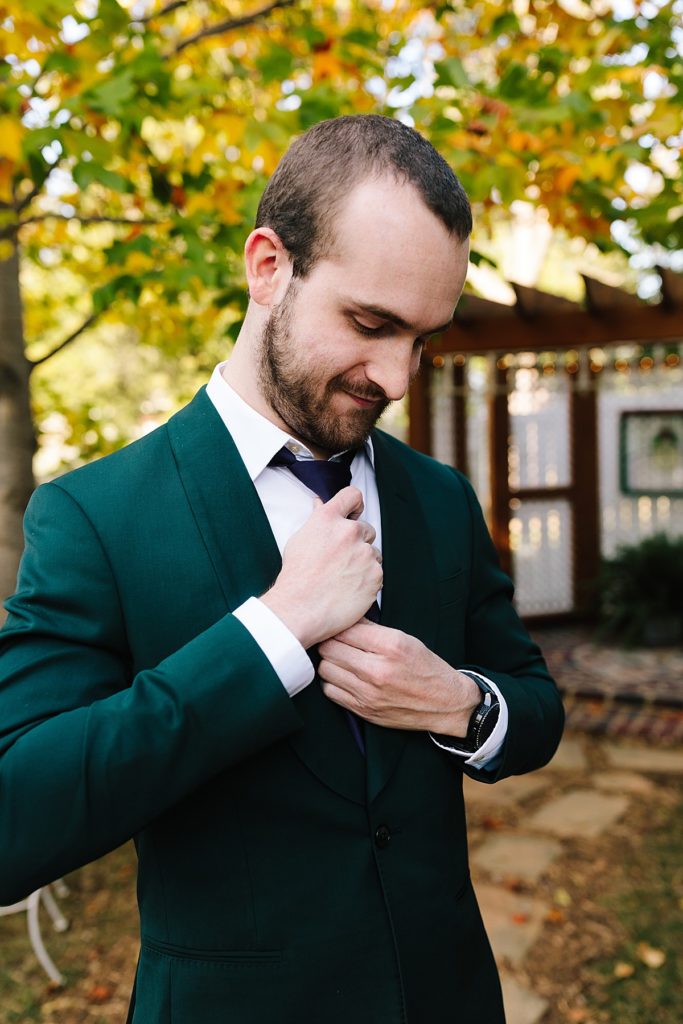 groom wearing a dark green suit from The Black Tux adjusts his purple tie