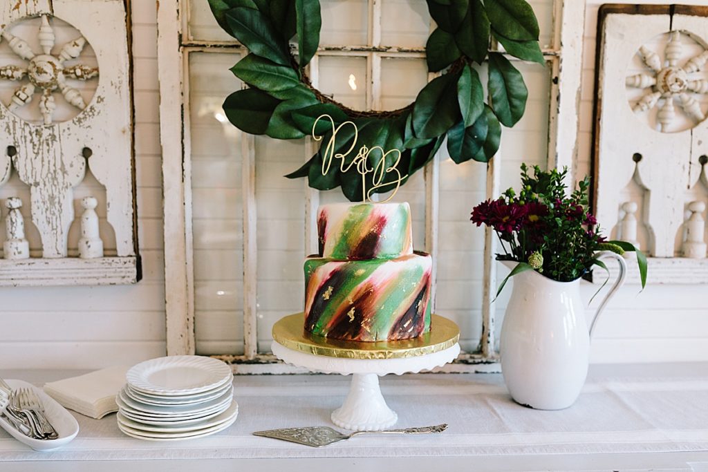 gluten free wedding cake decorated with hand painted watercolors in green, red, purple, and gold with a gold initial cake topper