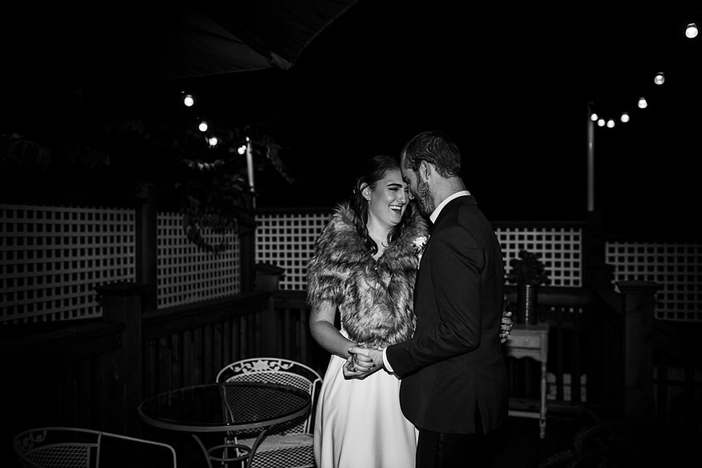 bride wears faux fur shawl during her first dance with her groom outside under string lights