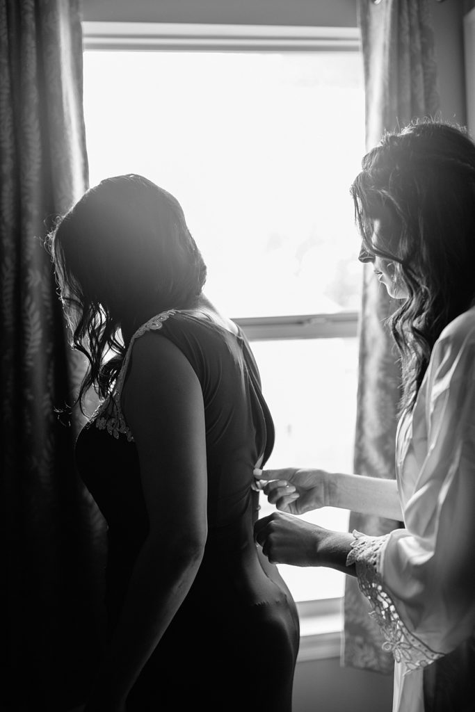 bride helps her mom with her dress by a sunlit window, a candid moment photographed by Kansas city photographer Natalie Nichole Photography