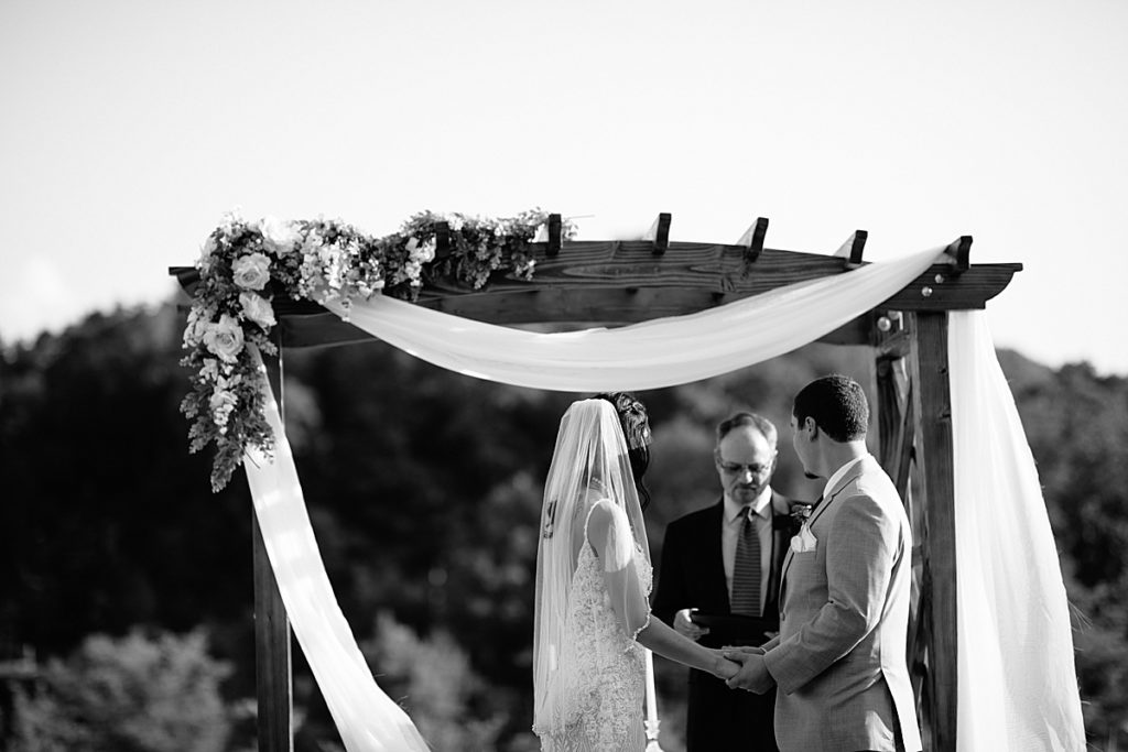 outdoor wedding ceremony with wooden arbor, fabric draping, and florals