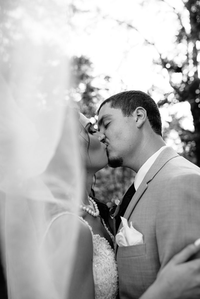 black and white photo of bride and groom kissing under the brides veil