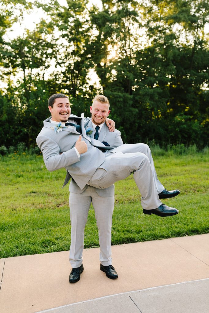 groomsmen picks up groom in their grey suits and navy vest for a fun wedding photo