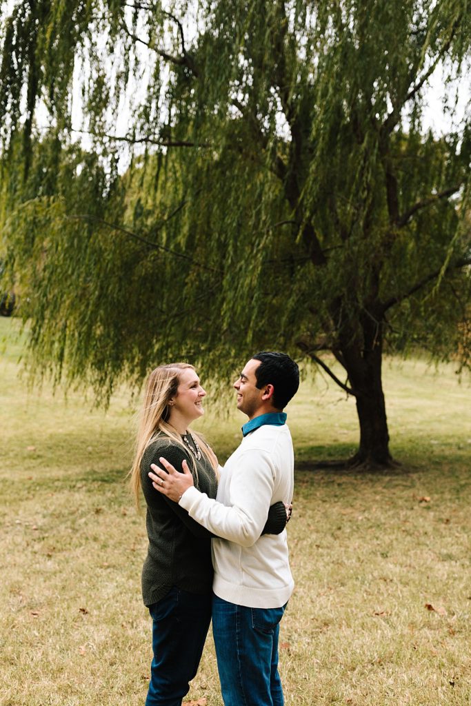 couple keeps each other warm in front of weeping willow tree in loose park