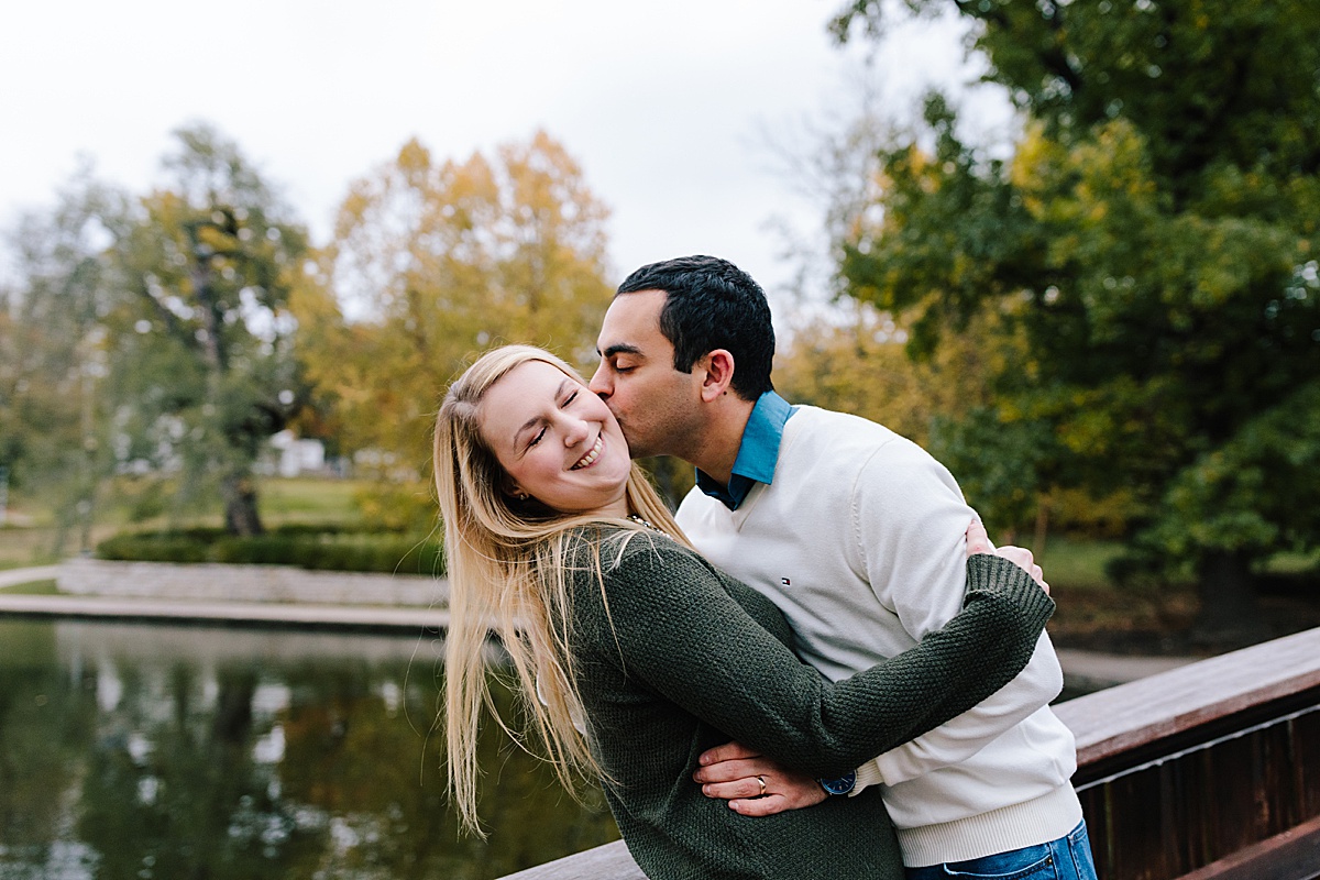 guy kisses girl on cheek near pond at loose park in kansas city for their fall couples photos