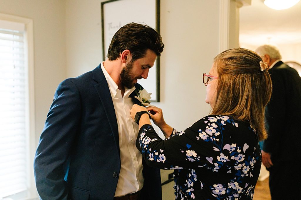 mother of the groom pins his white rose boutonniere to his navy suit jacket