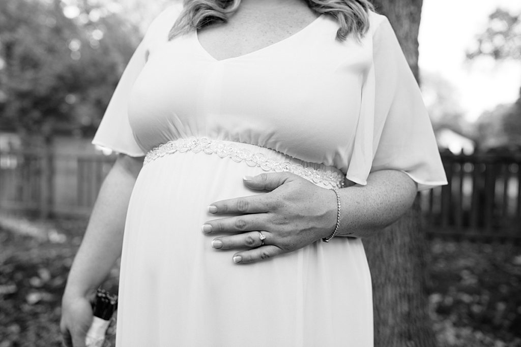 pregnant bride photo idea, bride places her hand on her stomach with her wedding ring wearing a simple belted wedding dress with flutter sleeves