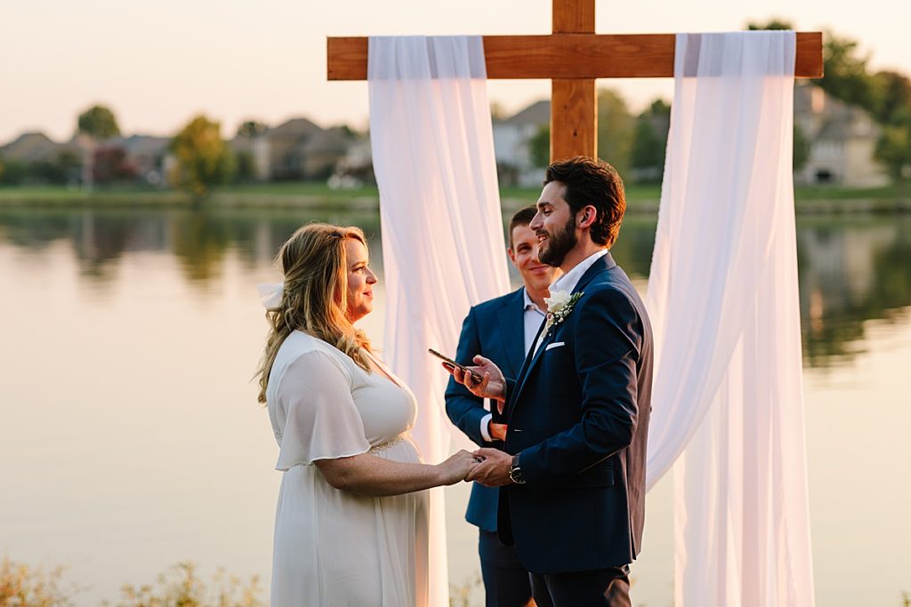 groom reads his vows to his wife at their outdoor wedding ceremony in Kansas City at Raintree Lake during golden hour in October