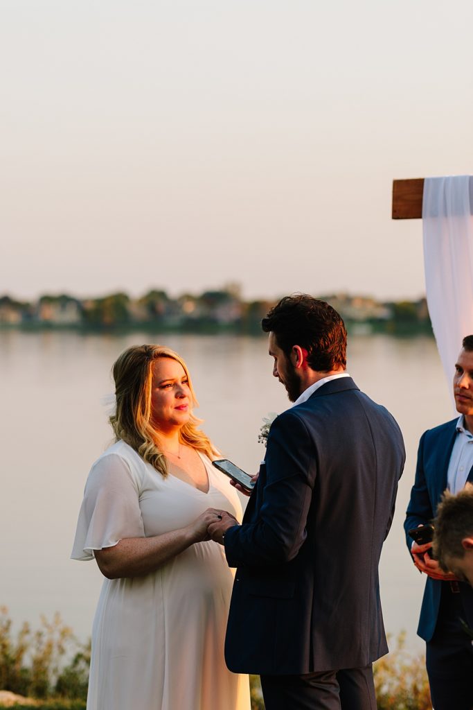 groom reads his vows to his wife at their outdoor wedding ceremony in Kansas City at Raintree Lake during golden hour in October