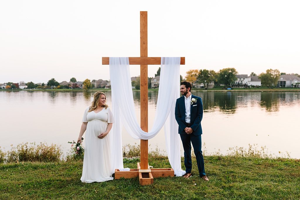 bride and groom with their large handmade wooden cross at their outdoor wedding ceremony on Raintree Lake in Kansas City, unique modern pose idea for bride and groom