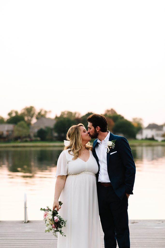 bride and groom kiss on the dock at the lake after their intimate elopement on the water after changing their large wedding into a small outdoor ceremony with just family