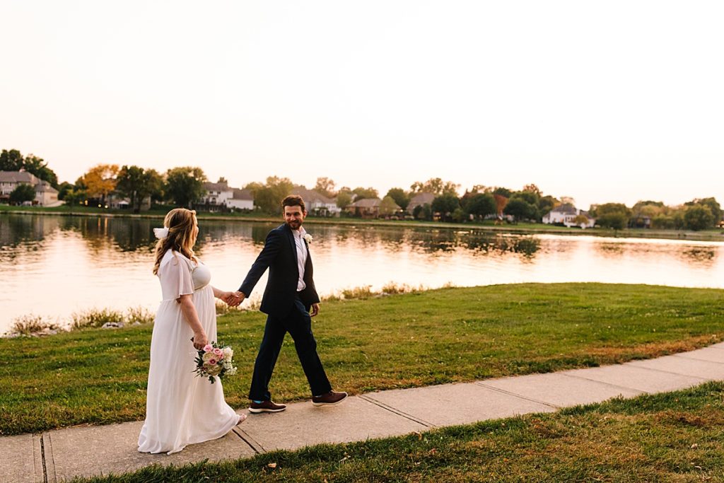 bride and groom walking by raintree lake as the sun sets after their backyard wedding in kansas city