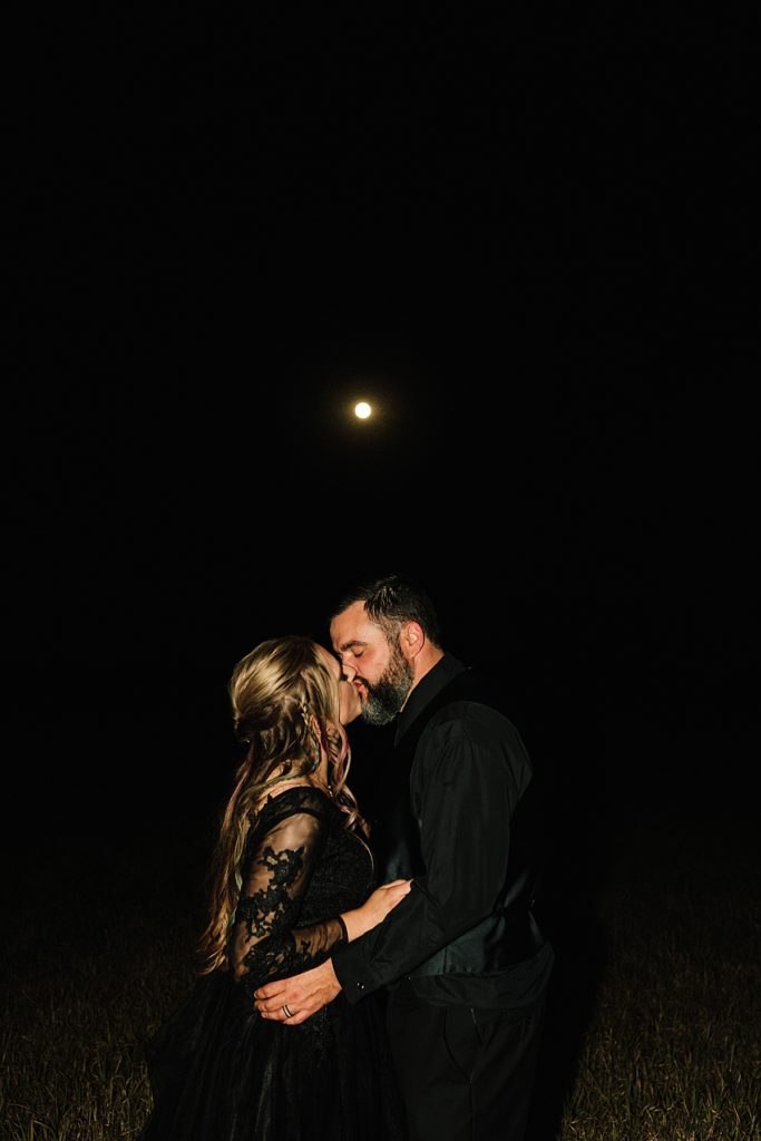 after dark photos, bride and groom with the full moon after their halloween wedding, bride wearing black lace wedding dress, groom wearing all black suit, groom attire, night time wedding portraits, flash wedding photography