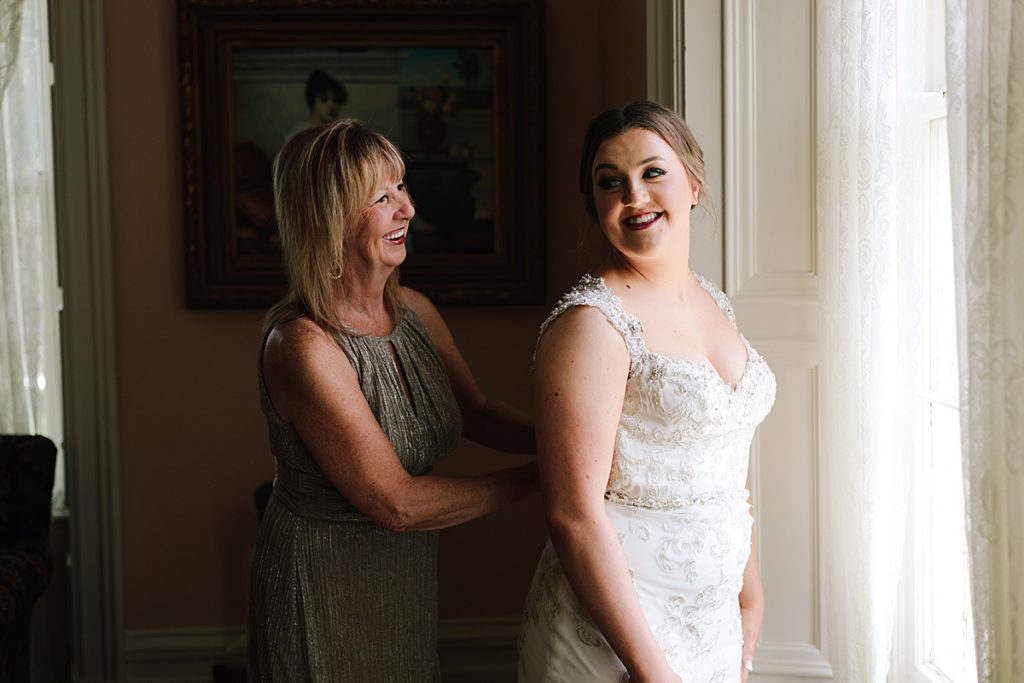 Choosing Your Getting Ready Space: Tips From a KC Wedding Photographer, wedding day, bride getting ready with her mom, mother of the bride zips up brides dress, shimmery mother of the bride dress, beaded wedding dress