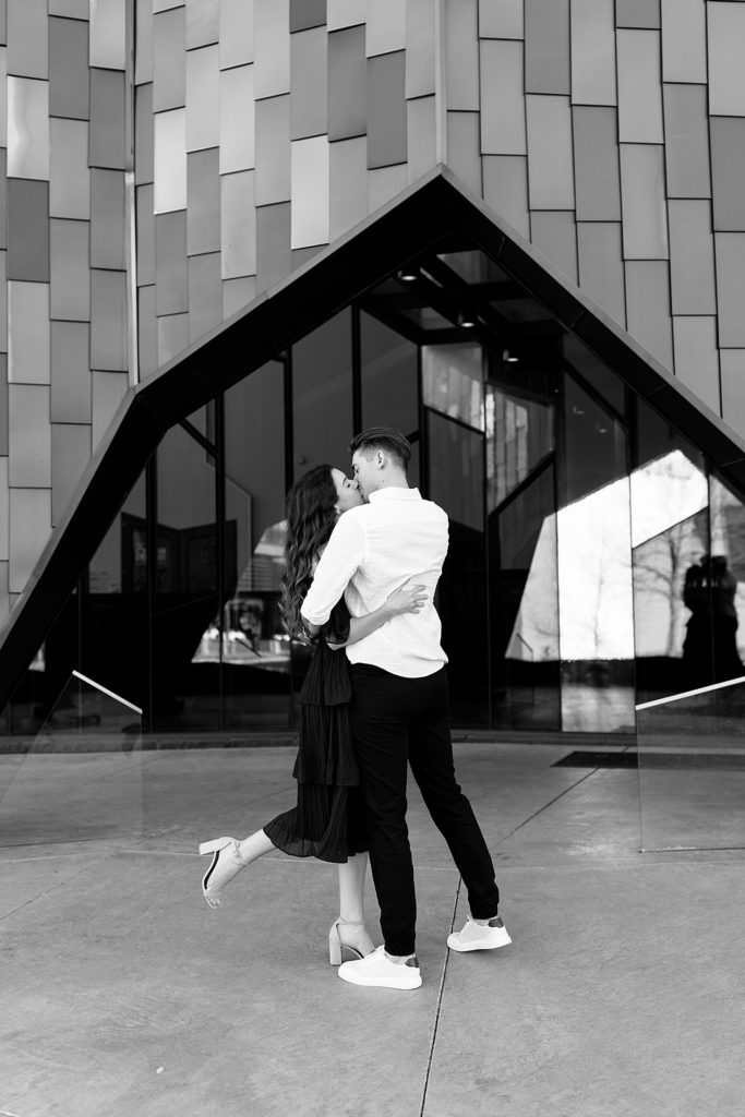 Black and white photo fo couple kissing in front of a building at their engagement session in Kansas City. 