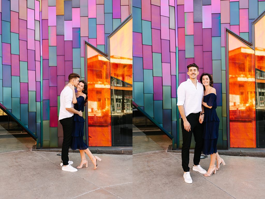 Engaged couple standing in front of a colorful building smiling for their engagement photos. 