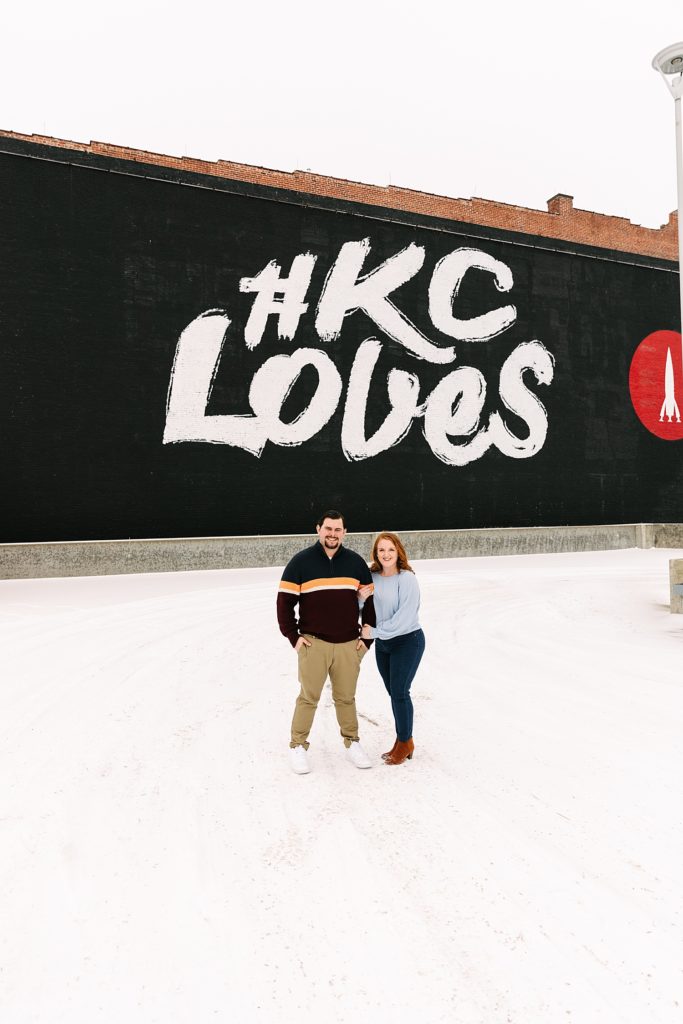 Man and woman posing in front of the KC Loves mural for their engagement session with Kansas City Photographer.