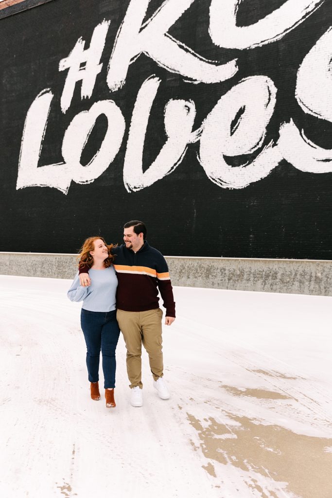 Couple waking close together towards the camera with the KC Loves Mural behind them.