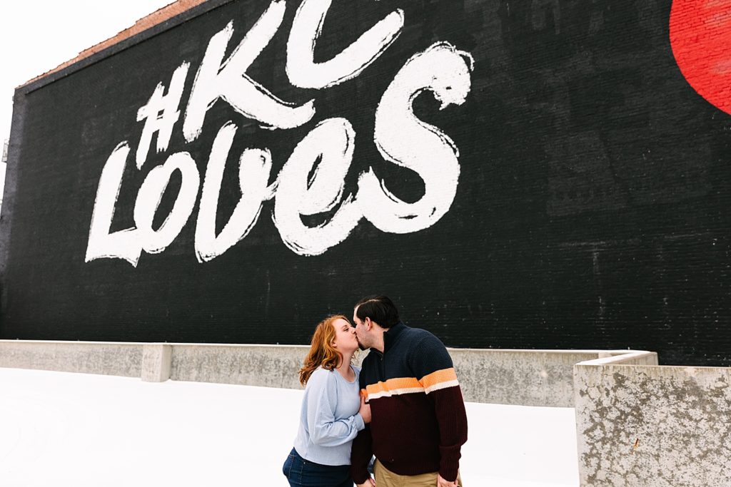 Man and woman kissing in front of the #KC Loves Mural. 