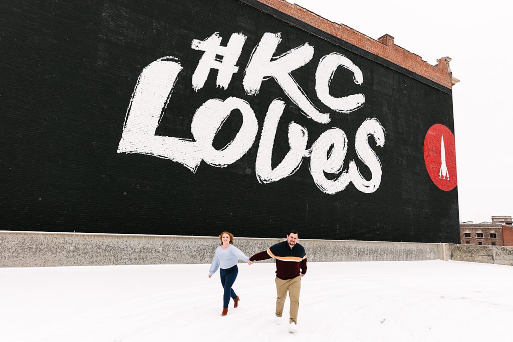 Man and woman running with the #KC Loves mural behind them. 