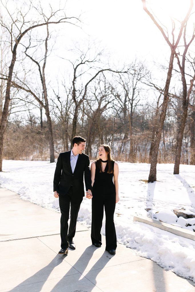 Man and woman laughing and walking down a pathway with snow all around them. 