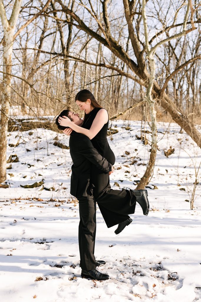 Man holding up woman for their engagement session in the snow. 