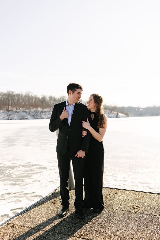 Man in suit and woman in black romper standing on the edge of a frozen lake. 