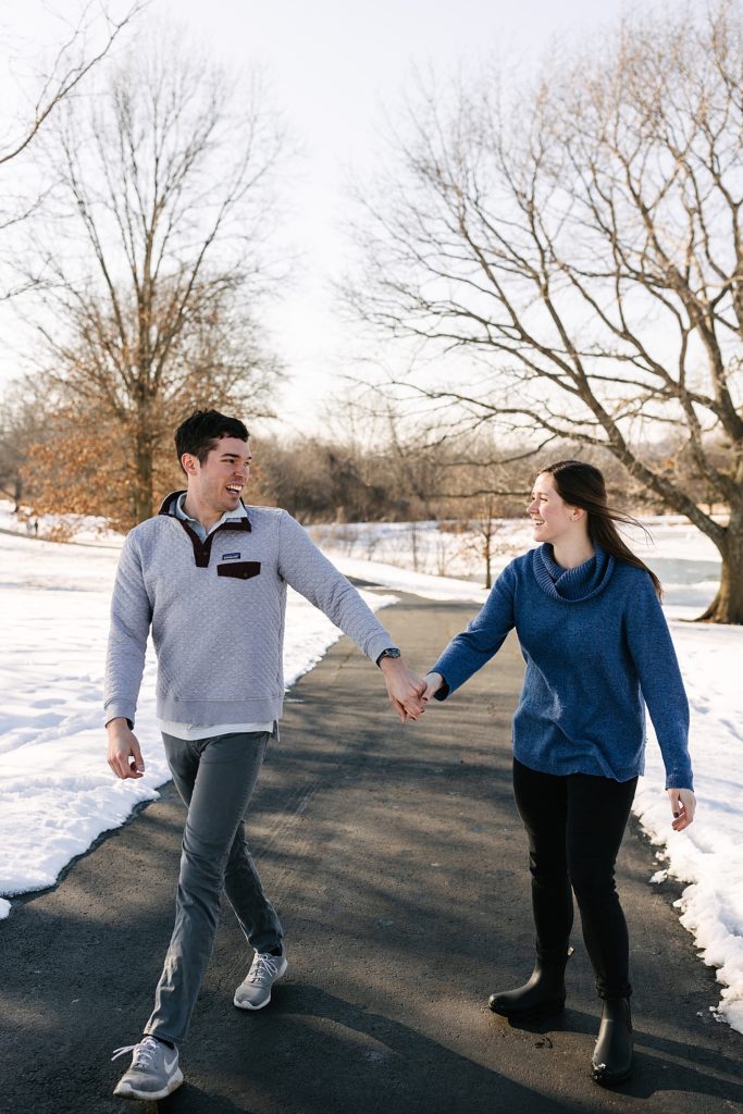 Man and woman in casual clothing walking down a pathway in the snow in Shawnee Mission Park. 