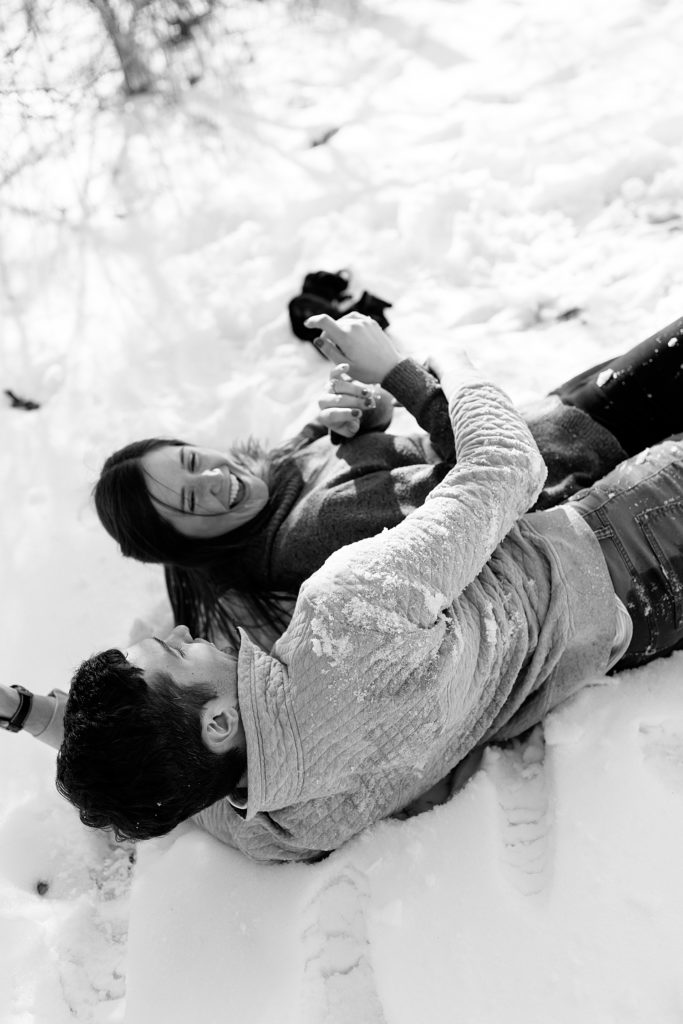 Black and white image of a man and woman falling over in the snow. 