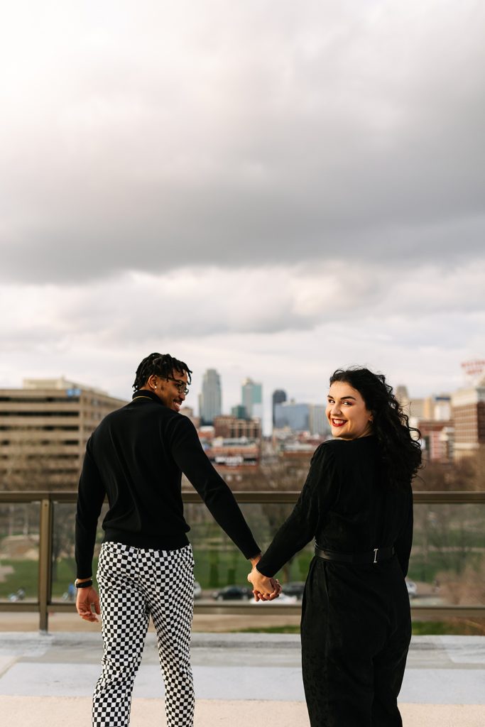 Man and woman walking away from the camera on a rooftop, woman is looking back and laughing. 