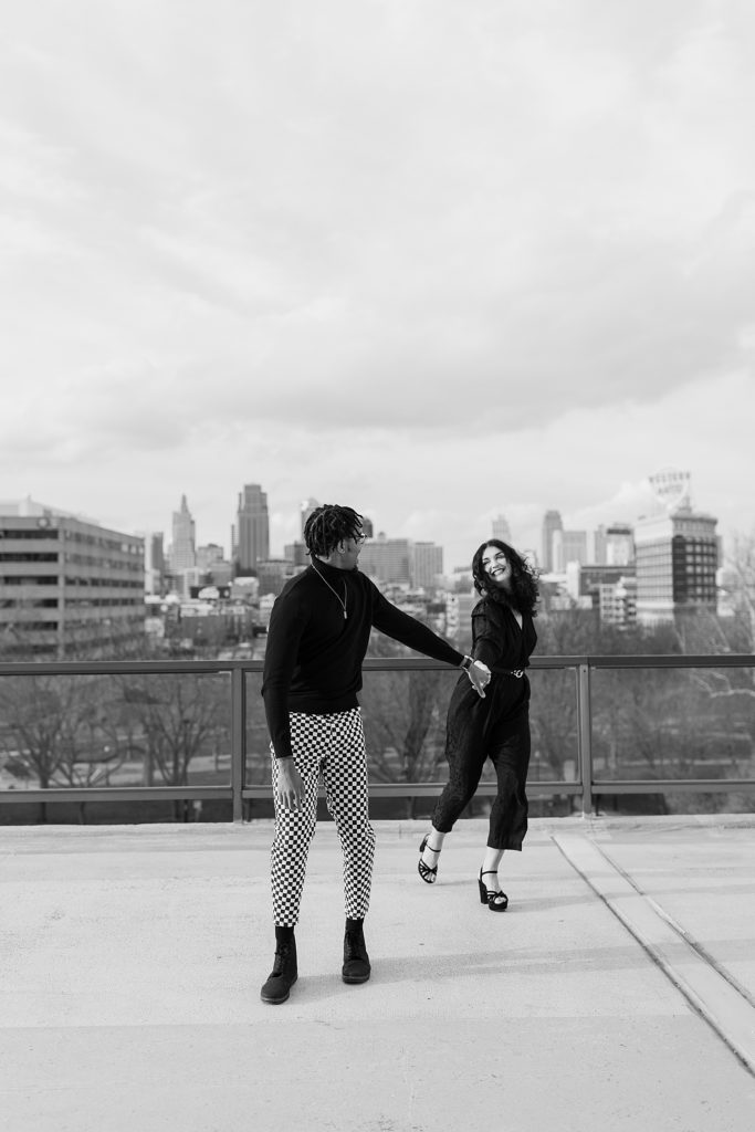 Black and white image of a woman and man laughing and walking towards the camera on a rooftop. 