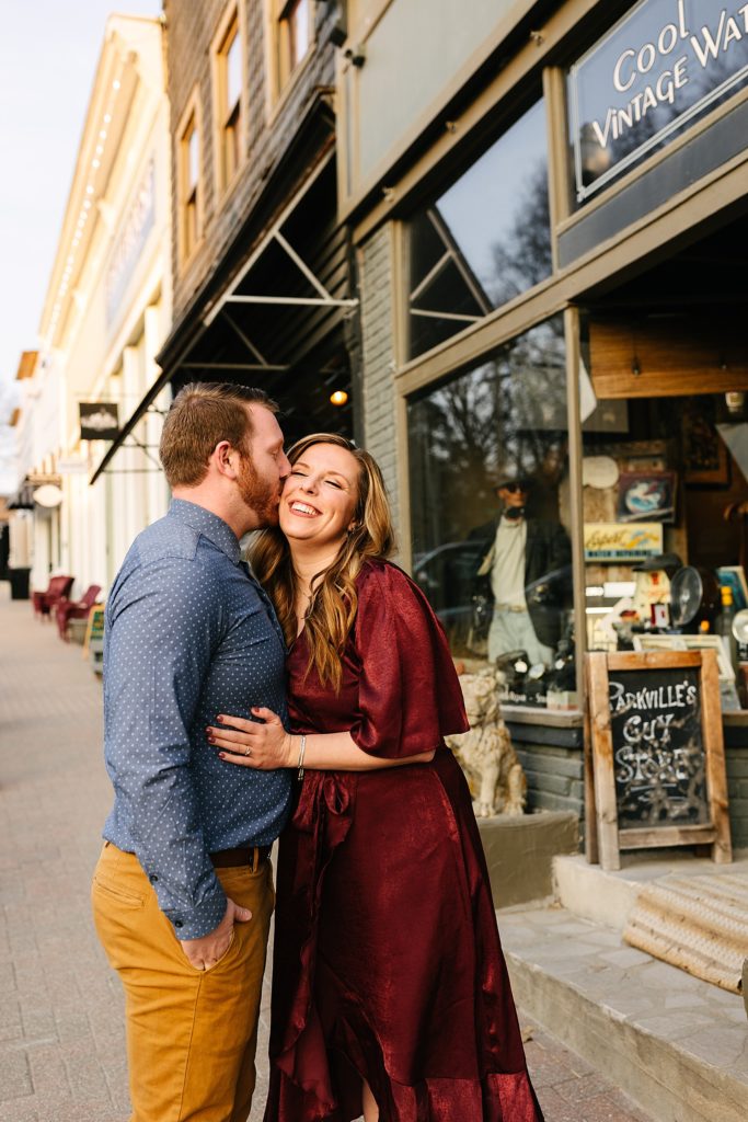 Man and woman in rich jewel tone clothes smiling and kissing on the street.