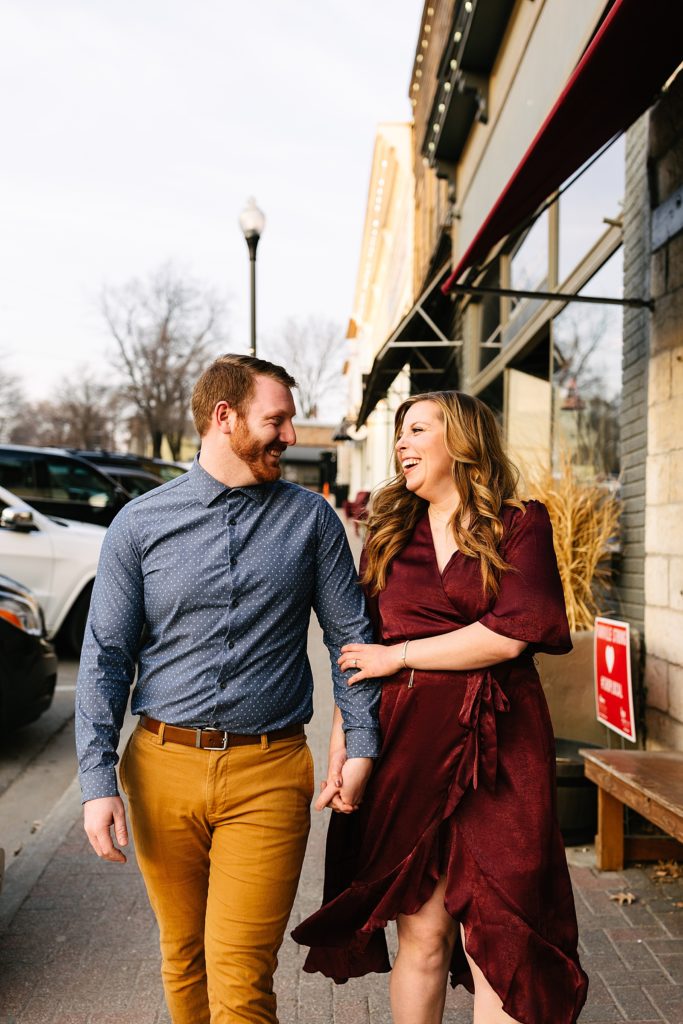 Engaged couple walking down the streets of Parkville, Missouri smiling at each other.