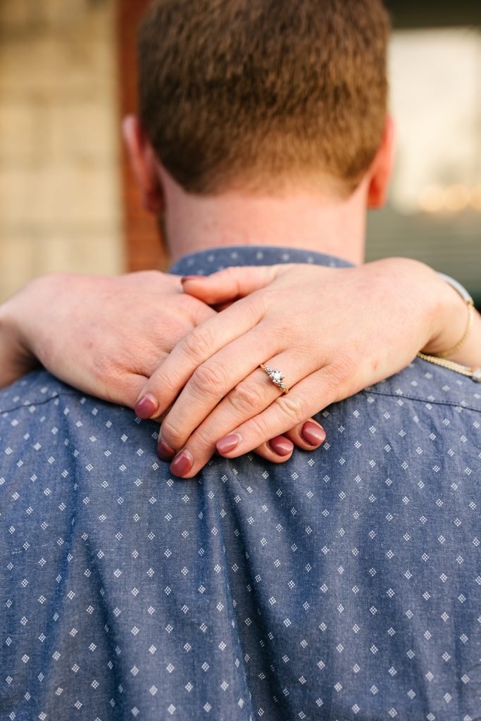 Detail shot of a woman's hand laced over her man's neck, with an engagement ring in focus.
