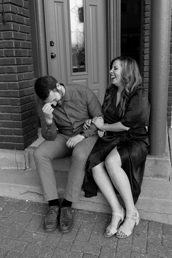 Black and white image of man and woman sitting on a doorstep, laughing out loud together. 