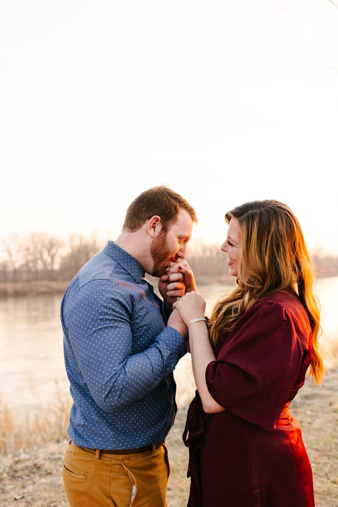 Man bringing his fiancé's hand up to his mouth to lovingly kiss her during their golden hour engagement session with Kansas City Photographer.
