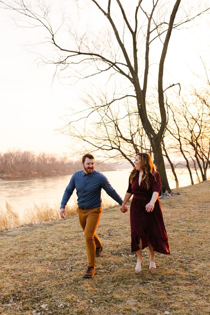 Man and woman in Fall colored clothing walking and laughing next to a river. 