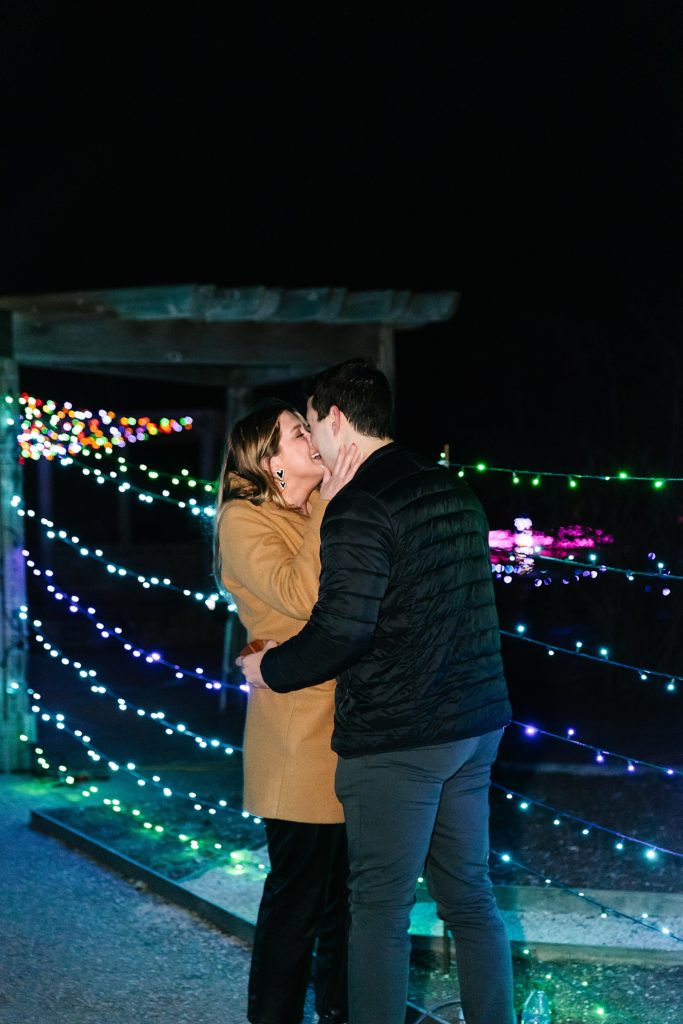 Man and woman kissing after Christmas lights proposal in December. 