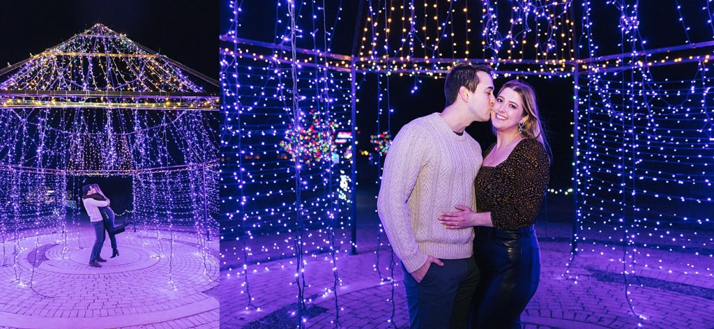 Newly engaged couple embracing while surrounded by Christmas lights.