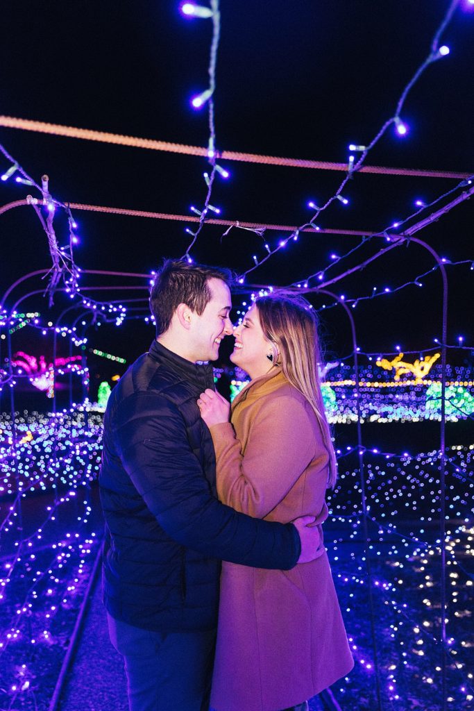 Man and woman embracing under Christmas lights.