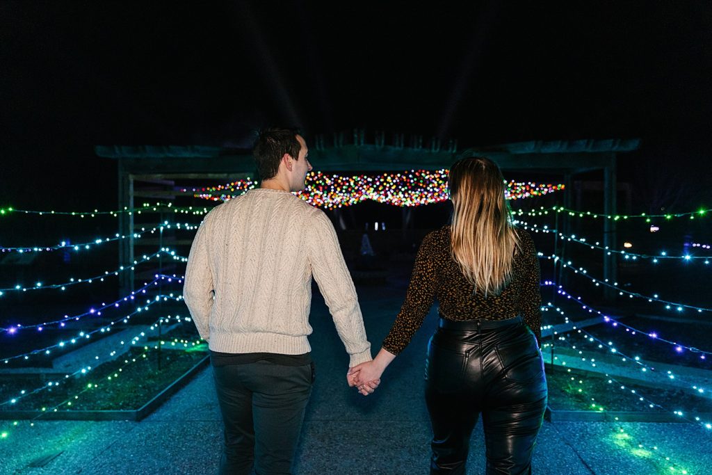 Newly engaged couple walking through lights after their Christmas lights proposal. 