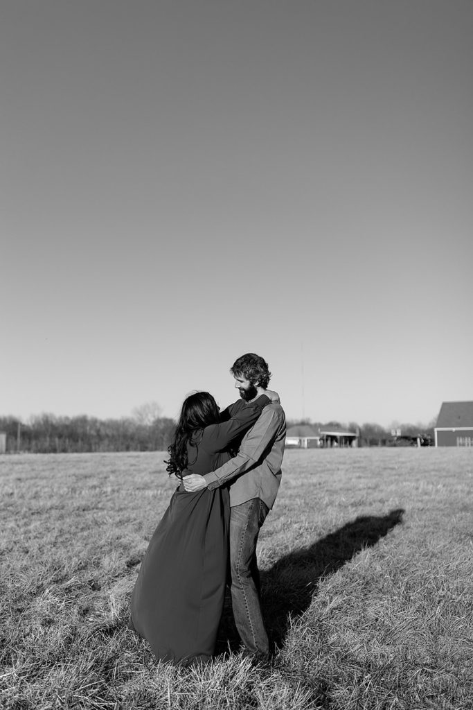 Black and white image of couple embracing in the middle of the field.